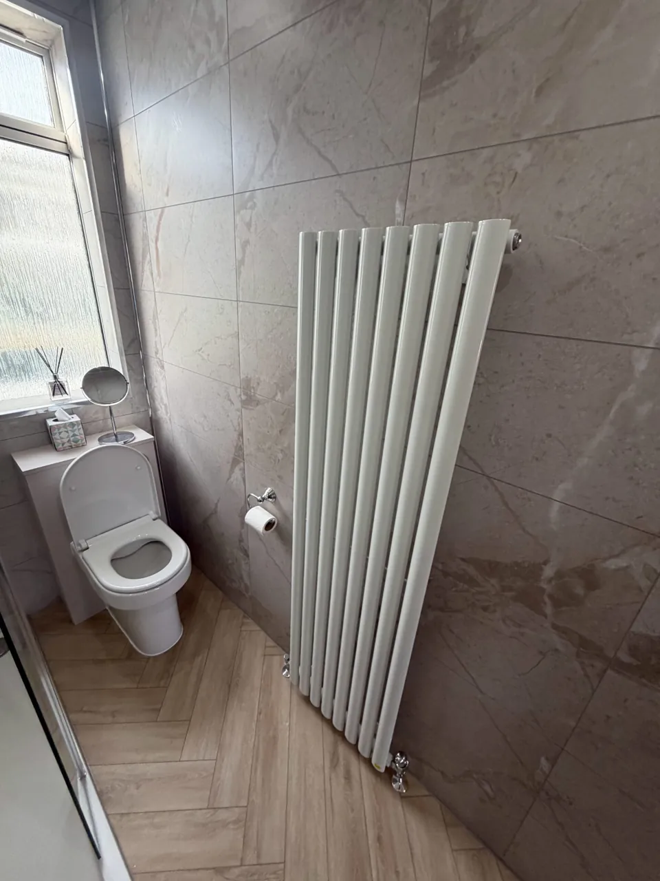 Tall white radiator beside marble-effect bathroom walls